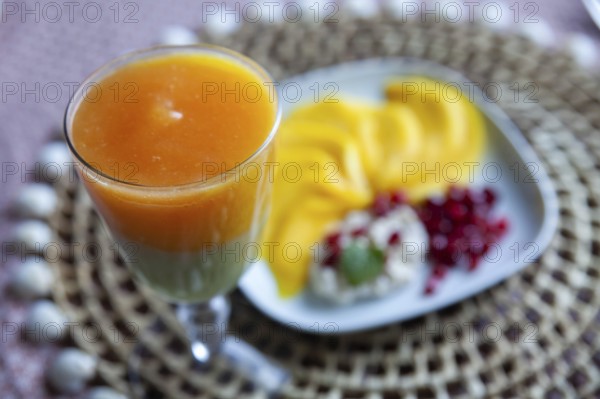 A glass with multi-coloured juice and a plate with mango slices and pomegranate seeds, Lower Austria Austria