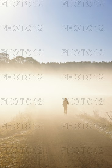 Person in silhouette running on a dirt road in autumn fog in the countryside
