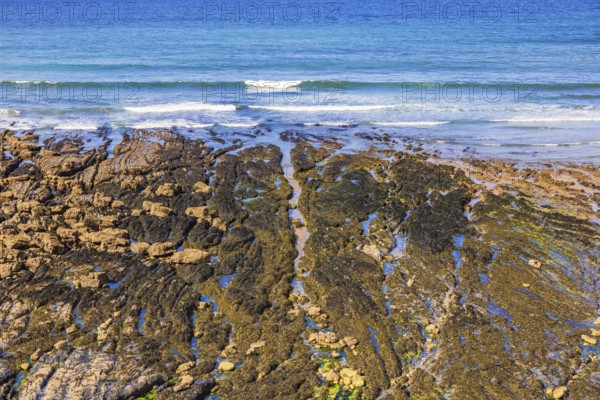 Beach by the sea at low tide with water pools and waves crashing on the shoreline a sunny summer day, Crozon peninsula, Bretagne, France
