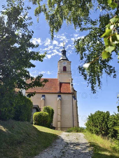 Church in the countryside with a tower on a sunny summer day, surrounded by trees and a path, Pöllau Styria Austria
