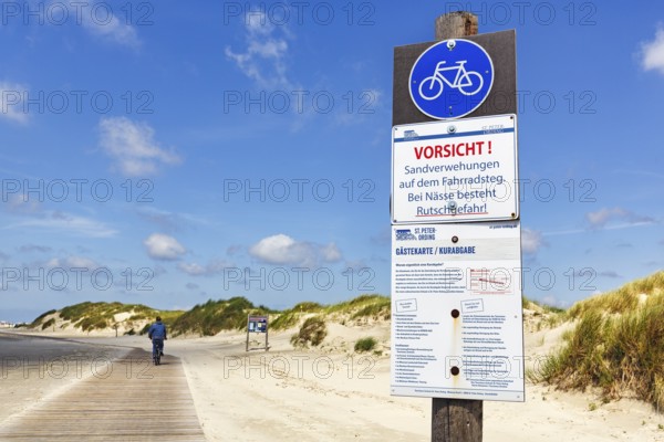 Cyclist on wooden path through the dunes to the sea, sign warns of wetness, danger of slipping and sand drifts on cycle path, Cumulus, Sankt Peter-Ording, Eiderstedt, Wadden Sea National Park, North Frisia, Schleswig-Holstein, Germany