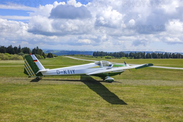Motor glider of the type Scheibe SF.25C Falke standing on Wasserkuppe airfield, in the background runway landing strip, Wasserkuppe airfield, Rhön, Gersfeld, district of Fulda, Hesse, Germany