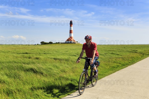 Cyclist, cycle tour through salt marshes, Westerheversand lighthouse on the horizon, Cirrus, Westerhever, Eiderstedt, North Frisia, Schleswig-Holstein, Germany