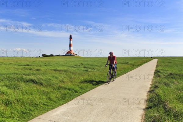 Cyclist, cycle tour through salt marshes, Westerheversand lighthouse on the horizon, Cirrus, Westerhever, Eiderstedt, North Frisia, Schleswig-Holstein, Germany