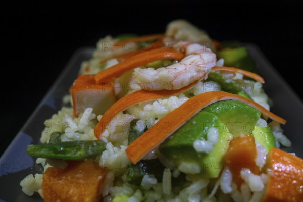 Rice salad with shrimp, red bell pepper and avocado, on black background