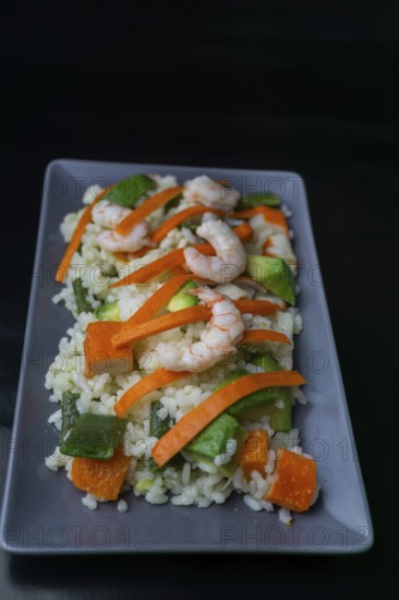 Rice salad with shrimp, red bell pepper and avocado, on black background