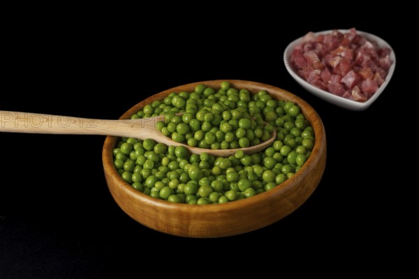 Wooden bowl with peas and white bowl with iberian ham isolated on black background