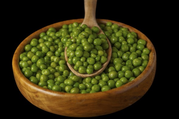 Wooden bowl with fresh peas and wooden spoon isolated on black background
