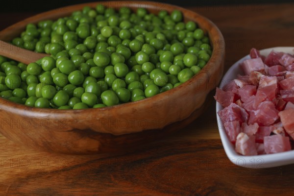 Wooden bowl with peas and white bowl with iberian ham isolated on black background