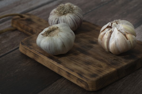 Whole and peeled garlic on wooden board and white background