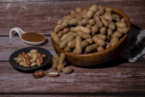 Peanuts in a wooden bowl and peeled peanuts on a plate with a spoonful of peanut butter