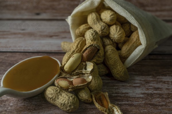 Peanuts in a raffia sack with a spoonful of peanut butter on a wooden bottom