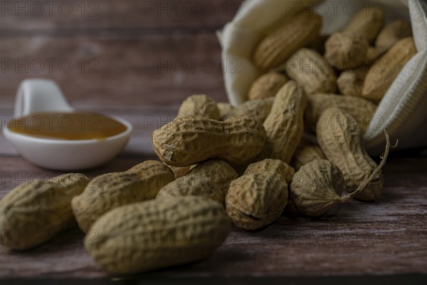 Peanuts in a raffia sack with a spoonful of peanut butter on a wooden bottom