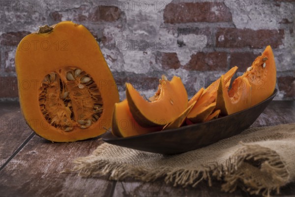 Split pumpkin in wooden bowl on raffia cloth
