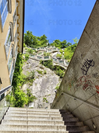 Modern stone staircase leads to a green rock under a clear sky, with graffiti stairs to the Graz Clock Tower Graz Styria Austria