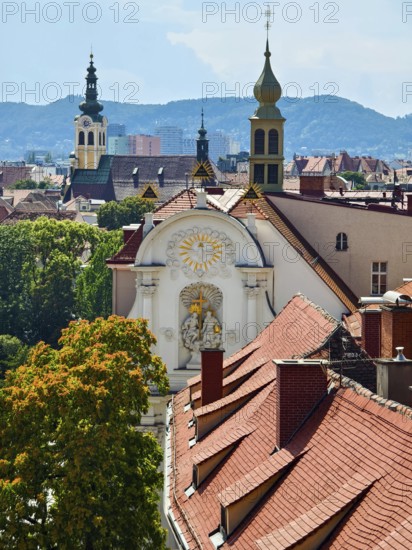 Panoramic view over the roofs of a historic city with church towers and mountains in the background Old town of Graz Styria Austria