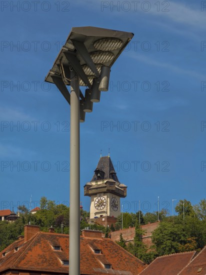 Clock tower behind a street lamp, surrounded by historic roofs and trees Graz Clock Tower Graz Styria Austria