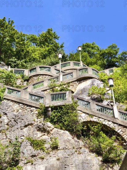 Stone wall with green railings and lamps on a steep, wooded slope under a blue sky Graz Styria Austria