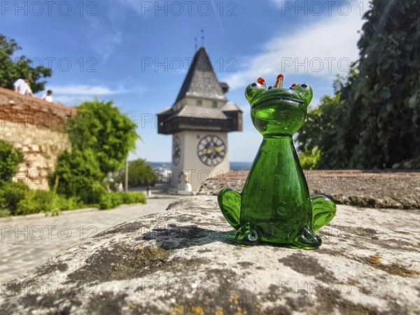 Green glass figure of a frog in front of historic clock tower