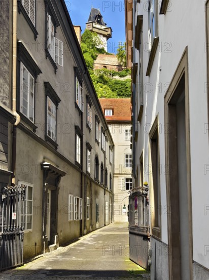 Narrow alleyway in the historic city centre, lined with old buildings with a tower in the background Graz clock tower Graz Styria Austria