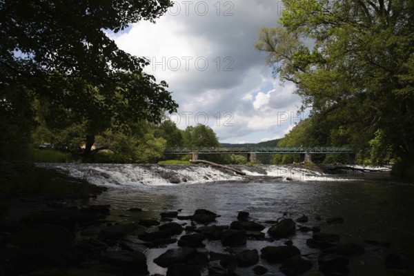 A forested stretch of river with a bridge and waterfall under a cloudy sky Hardegg Weinviertel Lower Austria