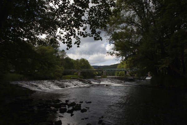 A dark river with a waterfall and bridge, surrounded by forests and cloudy skies Hardegg Weinviertel Lower Austria