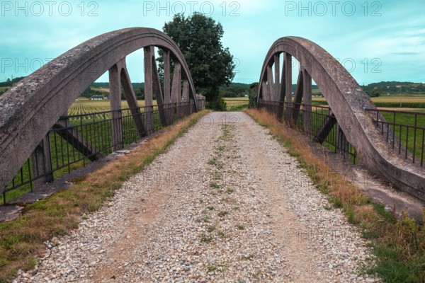An old bridge with a gravel path leads through a rural area, surrounded by fields and a clear sky Perschling flood channel bridge Lower Austria Austria