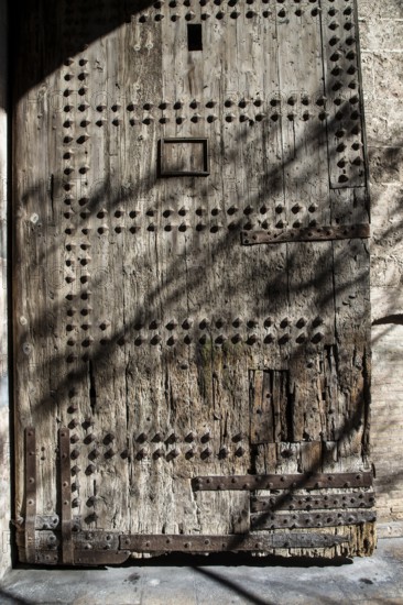 A solid, antique wooden door full of texture and nails