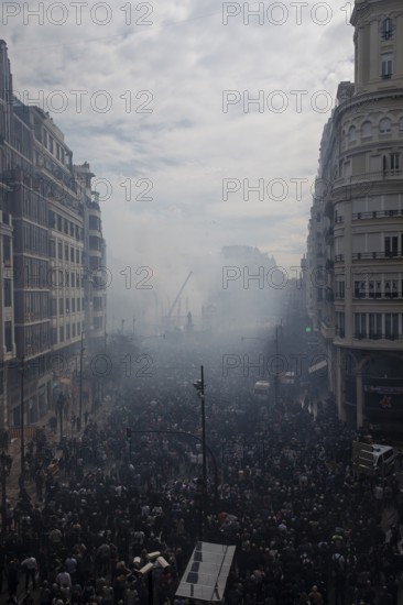 A large crowd gathers in a smoky city street Mascletá de Fallas