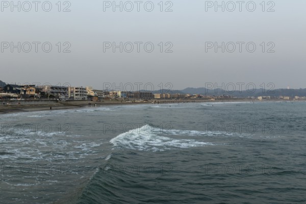 Houses on the seafront and surfers in the surf at dusk on the beach in Kamakura, Kanagawa Prefecture, Japan