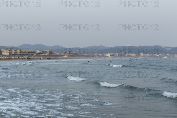 Houses on the seafront and surfers in the surf at dusk on the beach in Kamakura, Kanagawa Prefecture, Japan