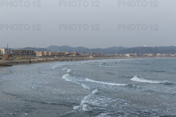 Houses on the seafront and surfers in the surf at dusk on the beach in Kamakura, Kanagawa Prefecture, Japan