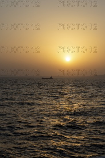 Background image, setting sun with silhouette of ship and land, water surface in evening light, waves in the sea at sunset, Tokyo Bay, Japan