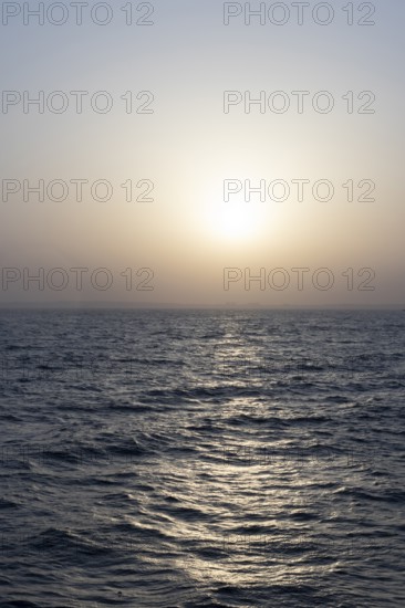 Background image, setting sun with silhouette of land, water surface in evening light, waves in the sea at sunset, Tokyo Bay, Japan