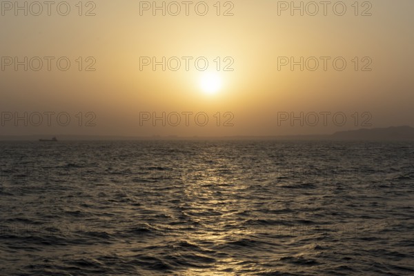Background image, setting sun with silhouette of land, water surface in evening light, waves in the sea at sunset, Tokyo Bay, Japan