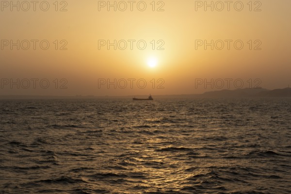 Background image, setting sun with silhouette of ship and land, water surface in evening light, waves in the sea at sunset, Tokyo Bay, Japan