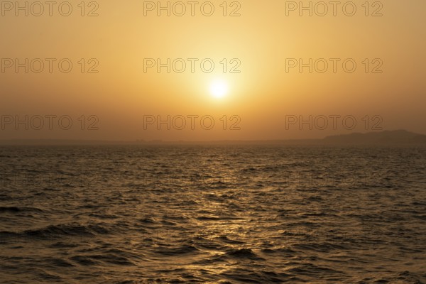 Background image, setting sun with silhouette of land, water surface in evening light, waves in the sea at sunset, Tokyo Bay, Japan