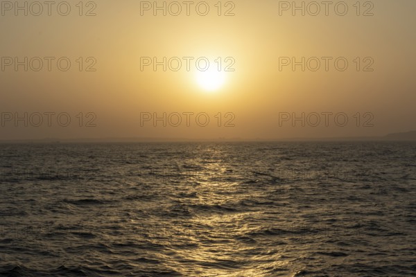Background image, setting sun with silhouette of land, water surface in evening light, waves in the sea at sunset, Tokyo Bay, Japan