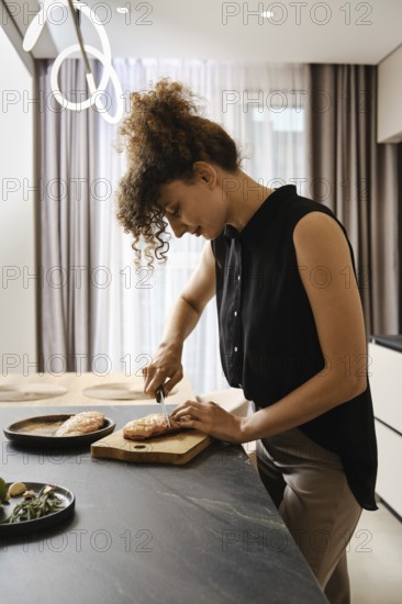 A woman is focused on cutting duck fat in a kitchen. Natural light fills the space, enhancing the inviting atmosphere as she prepares a delicious breakfast