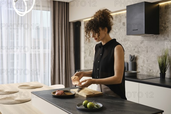 The woman holds in her hands a fresh raw duck breast. She is going to cook lunch in the kitchen