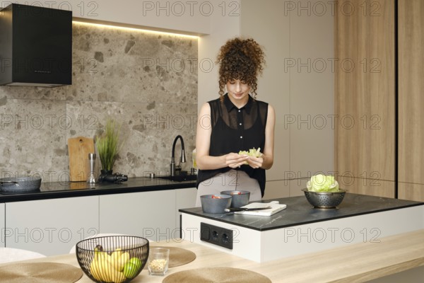 A woman wearing a stylish top works in a contemporary kitchen, skillfully preparing fresh lettuce. Natural light highlights the sleek design, creating an inviting atmosphere for healthy meal prep