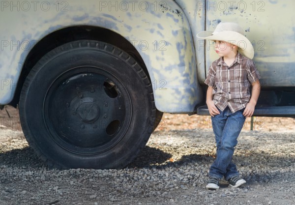 Young boy wearing cowboy hat relaxing leaning against antique truck