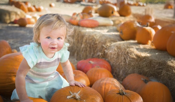 Cute baby girl having fun at the pumpkin patch on a sunny fall day