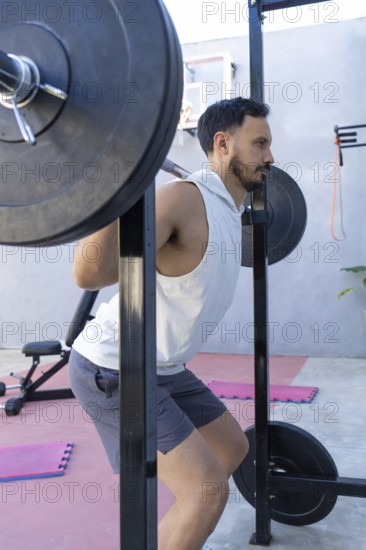 Focused male athlete is strengthening his legs by performing squats with a weighted barbell in a modern outdoor gym, showcasing dedication to fitness and a healthy lifestyle