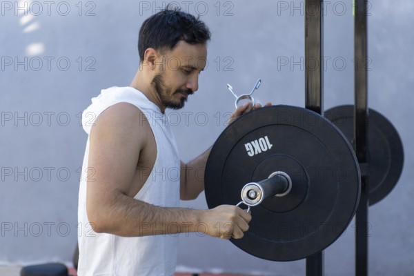 Focused male athlete meticulously secures weight plates onto a barbell, preparing for an intense strength training workout, showcasing dedication and commitment to physical fitness