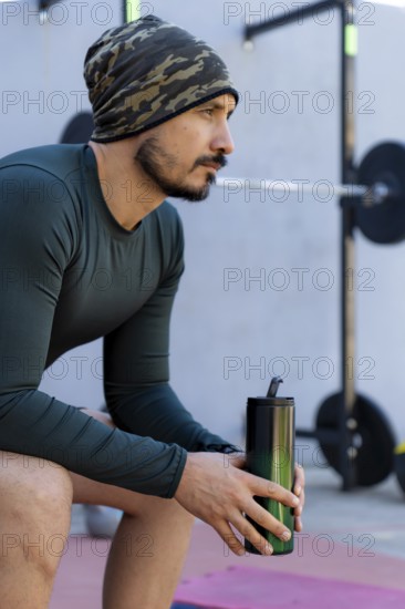 Athlete sitting and taking a break after an intense workout, holding a water bottle and emphasizing the crucial role of hydration in maintaining fitness and overall health