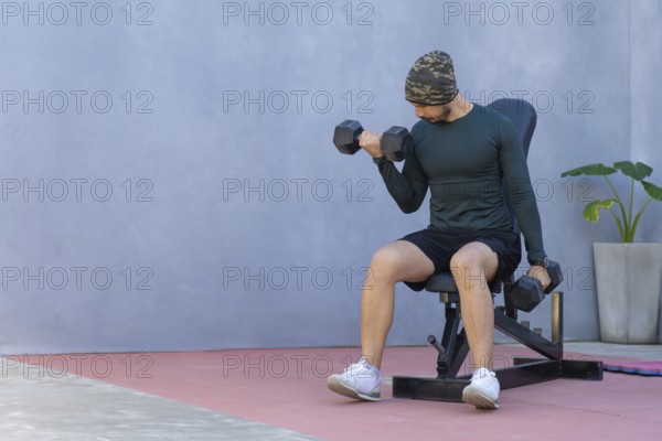 Focused athlete performs bicep curls with dumbbells, seated on a weight bench, showcasing dedication to strength training and physical fitness