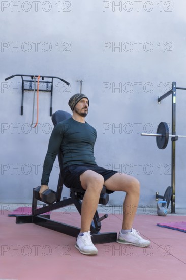 Athlete is strengthening his deltoids by performing seated lateral raises with dumbbells in an outdoor gym, demonstrating dedication and focus on physical fitness