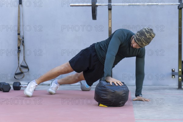 Focused male athlete wearing a beanie performing one-handed push-ups on a medicine ball in an outdoor gym, showcasing strength and dedication to fitness