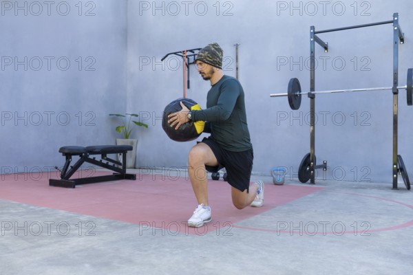 Athlete performing lunges while gripping a medicine ball in an outdoor gym, demonstrating strength and balance during an intense workout session focused on fitness and endurance